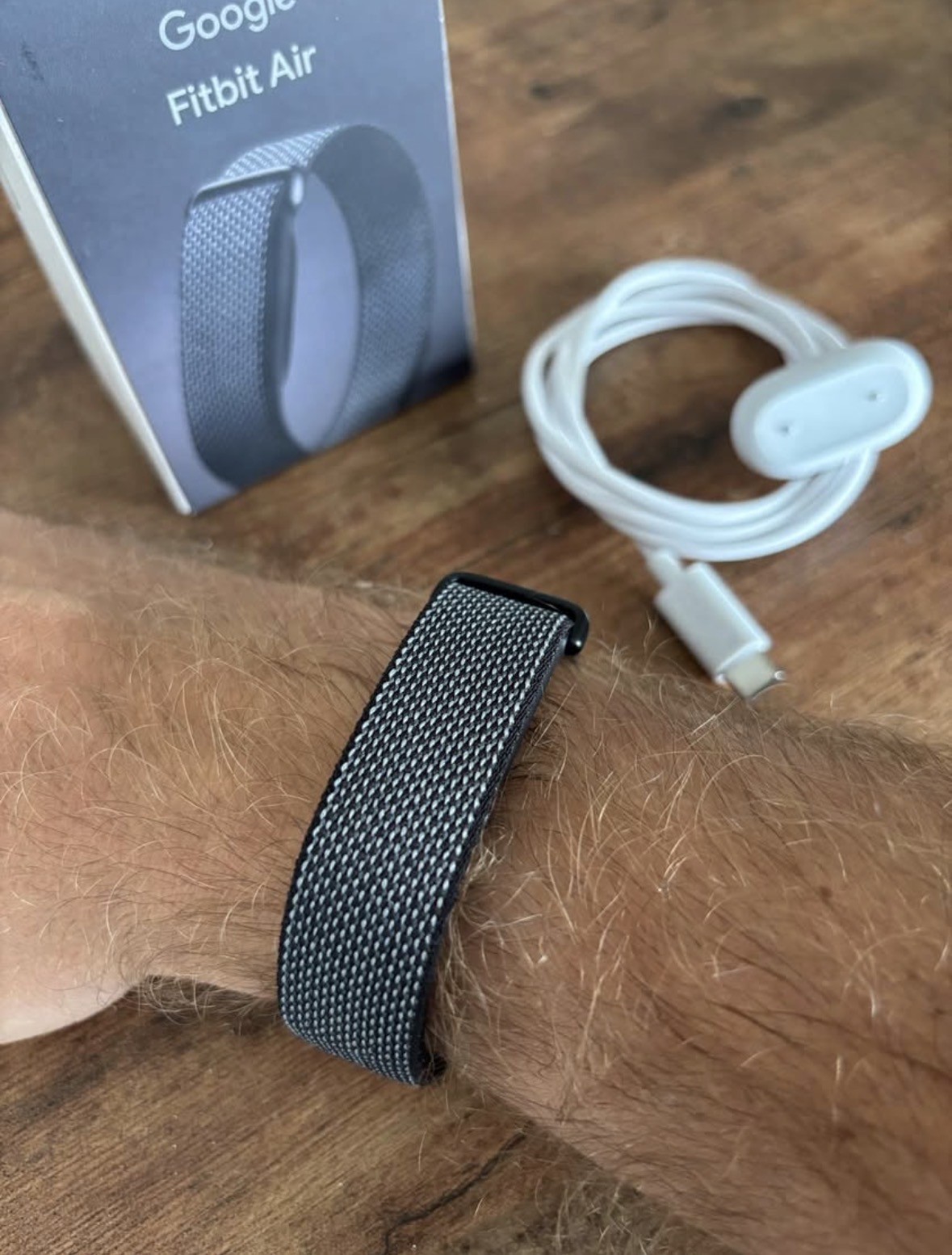 Fitbit Air na zápěstí vedle krabičky a nabíječky