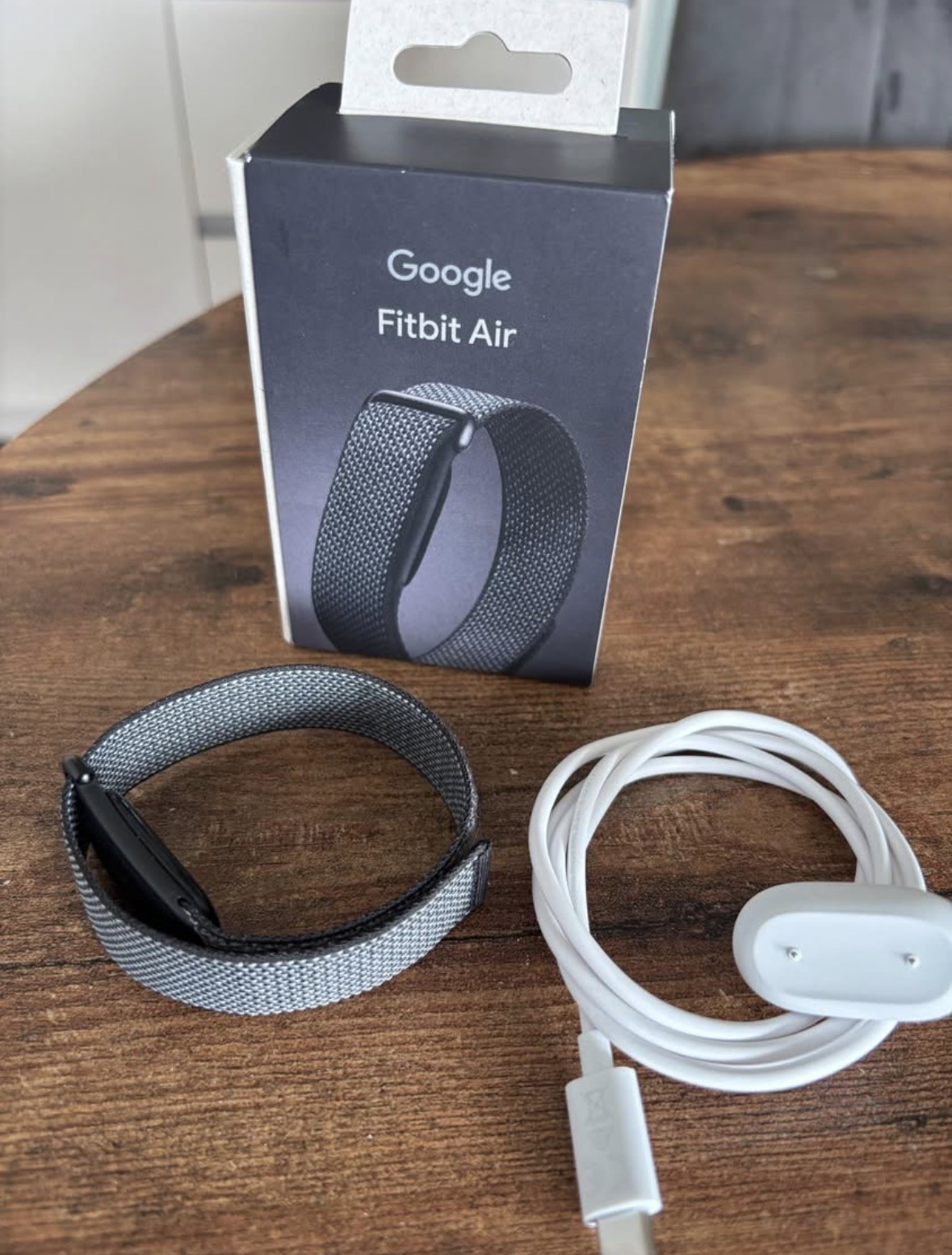 Rozbalený Google Fitbit Air — krabička, látkový náramek a nabíjecí kabel
